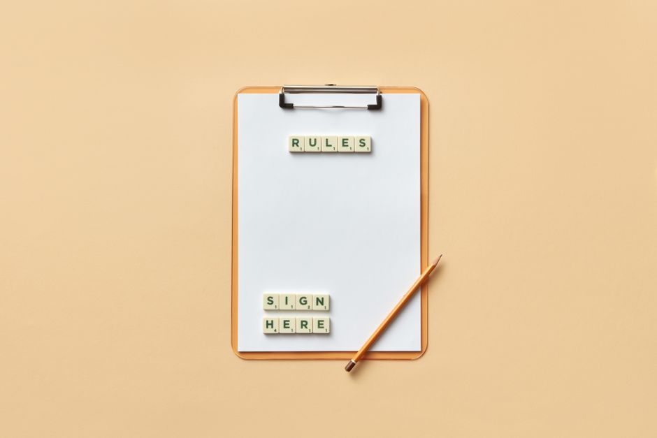 Flat lay of clipboard with letter tiles spelling 'rules' and 'sign here', accompanied by pencil on beige background.